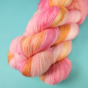 A couple of Sparkle yarn skeins that are colored with a light pink, yellow, and orang e, on top of a light blue background.