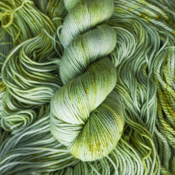 Sparkle yarn colored with different shades of light green and white with some dark green speckles on top of the same unwound yarn.