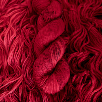 A vibrant red colored Sport yarn with some dark speckles, on top of an unwound version of that same yarn.
