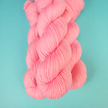 A light pink colored Sport yarn on top of a light blue background.
