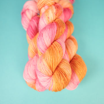 A couple of Sport yarn skeins that are colored with a light pink, yellow, and orang e, on top of a light blue background.