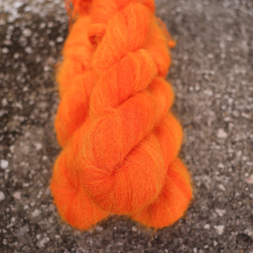 A couple of vibrant orange Suri yarn skeins on top of gravel.