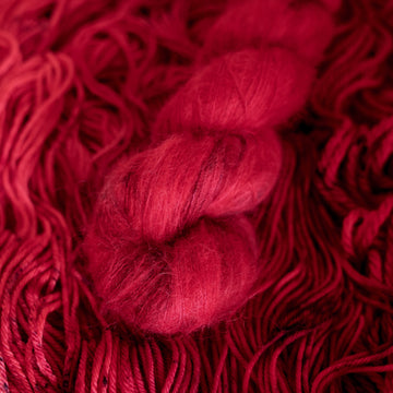A vibrant red colored Suri yarn with some dark speckles, on top of an unwound version of that same yarn.