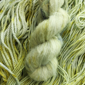Suri yarn colored with different shades of light green and white with some dark green speckles on top of the same unwound yarn.