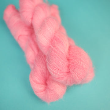 A light pink colored Suri Lace yarn on top of a light blue background.