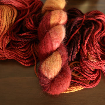 Suri yarn with red orange and yellow colors, on top of an unwound version of that same yarn. all on top of a dark wooden table.