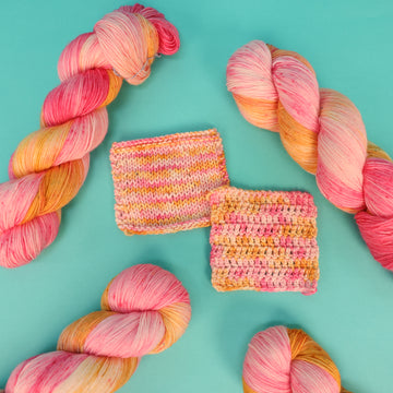 A couple of yarn skeins that are colored with a light pink, yellow, and orange, and knit and crochet swatches, on top of a light blue background.