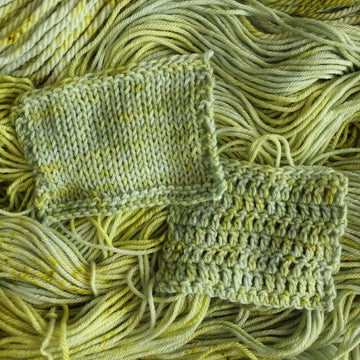 Knit and crochet swatches colored with different shades of light green and white with some dark green speckles on top of the same unwound yarn.