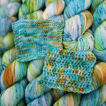 Crochet and Knit swatches with light shades of blue and speckles of purple, with some light greens and browns. There are more skeins like this of different weights underneath.