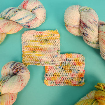 A light cream colored yarn with different colored speckles all over and banana colored yellow at the top of the skein and knit and crochet swatches of that yarn, on top of a light blue background.