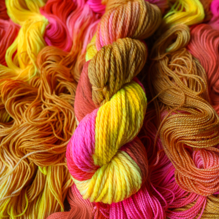 Bulky yarn colored a bright yellow, gpink, and a salmon pink orange, also a yellow beige color. This skein is on top of unwound skeins of this colorway.