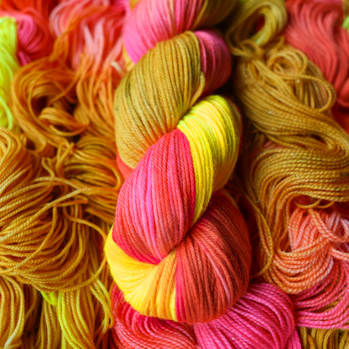 DK yarn colored a bright yellow, pink, and a salmon pink orange, also a yellow beige color. This skein is on top of unwound skeins of this colorway.
