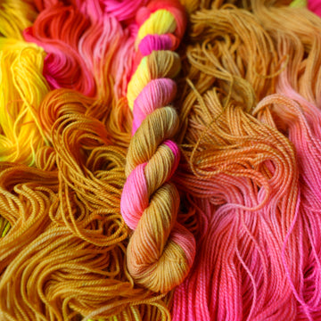Fingering mini yarn colored a bright yellow, pink, and a salmon pink orange, also a yellow beige color. This skein is on top of unwound skeins of this colorway.