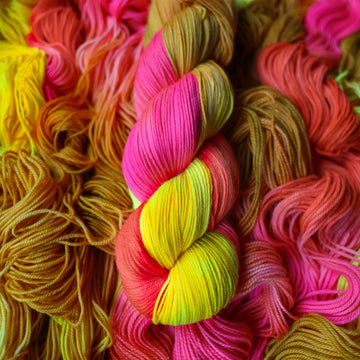 Fingering yarn colored a bright yellow, pink, and a salmon pink orange, also a yellow beige color. This skein is on top of unwound skeins of this colorway.