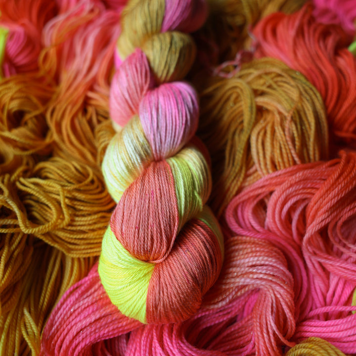 Silk yarn colored yellow, pink, and a salmon pink orange, also a yellow beige color. This skein is on top of unwound skeins of this colorway.