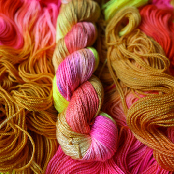 Silk DK yarn colored a bright yellow, pink, and a salmon pink orange, also a yellow beige color. This skein is on top of unwound skeins of this colorway.