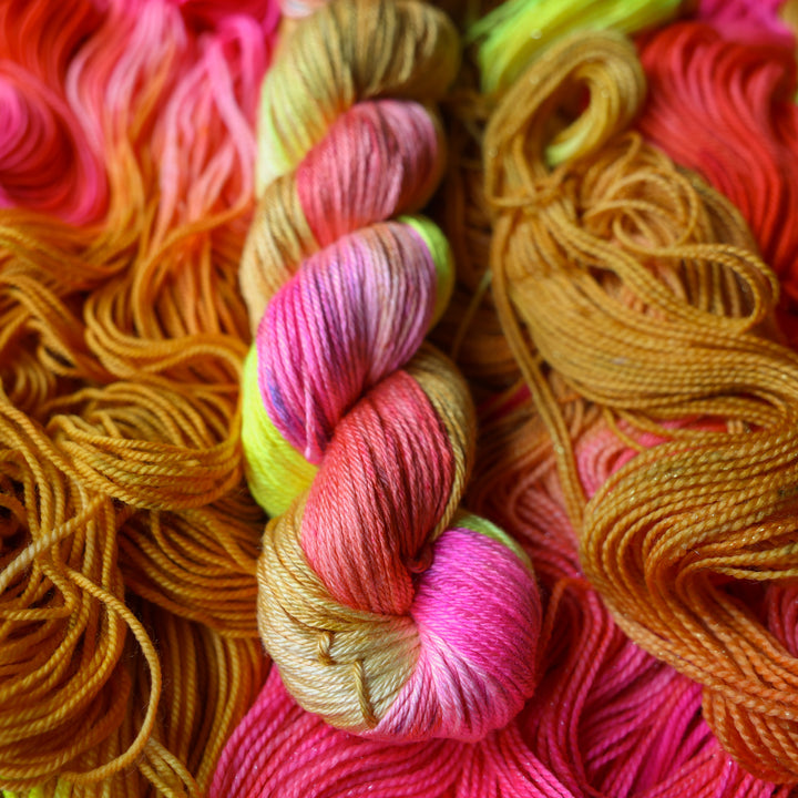 Silk DK yarn colored a bright yellow, pink, and a salmon pink orange, also a yellow beige color. This skein is on top of unwound skeins of this colorway.
