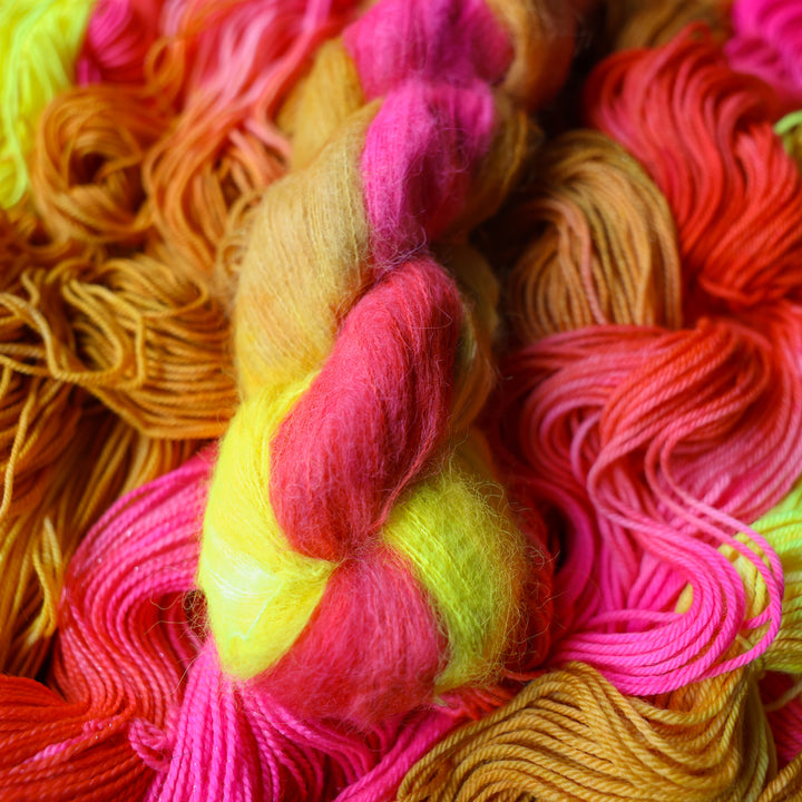Suri yarn colored a bright yellow, pink, and a salmon pink orange, also a yellow beige color. This skein is on top of unwound skeins of this colorway.