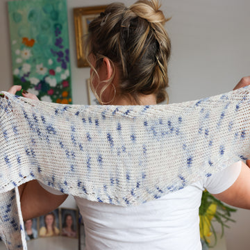 Women facing away wearing a Twisted Whispers Knit Shawl. The Shawl is white with hints of light blue details.
