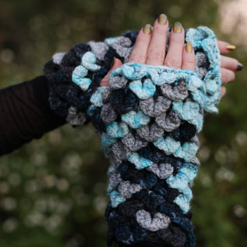 A shot of hands wearing Voidbane Mitts, a dragon scale crochet with icy blue, grey, dark blue and black colors.