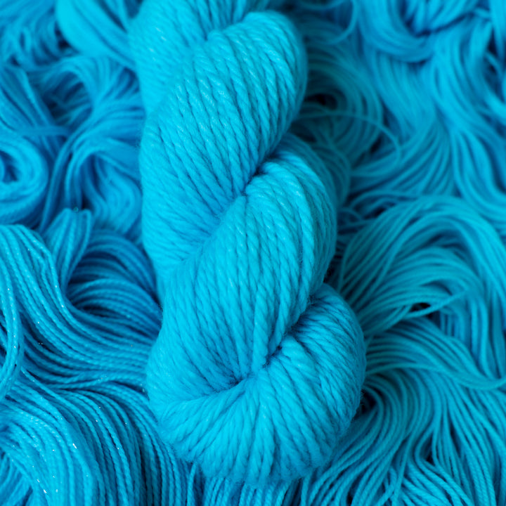 Bulky teal blue colored yarn skein on top of unwound skeins of this same color way