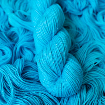 DK sparkle teal blue colored yarn skein on top of unwound skeins of this same color way