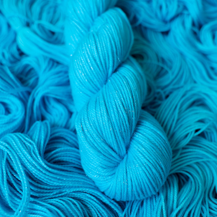 DK sparkle teal blue colored yarn skein on top of unwound skeins of this same color way