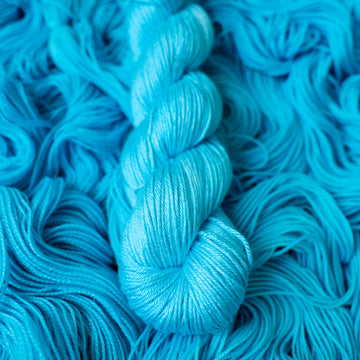 DK silk teal blue colored yarn skein on top of unwound skeins of this same color way