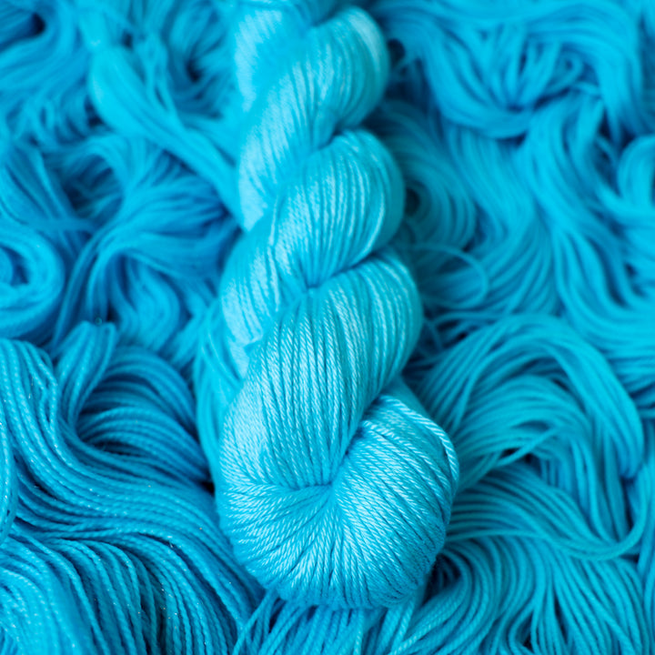 DK silk teal blue colored yarn skein on top of unwound skeins of this same color way