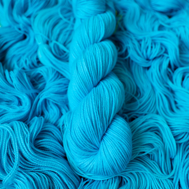 DK teal blue colored yarn skein on top of unwound skeins of this same color way