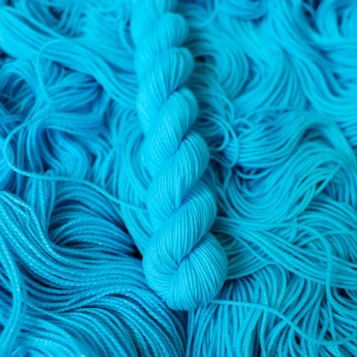 Fingering mini teal blue colored yarn skein on top of unwound skeins of this same color way