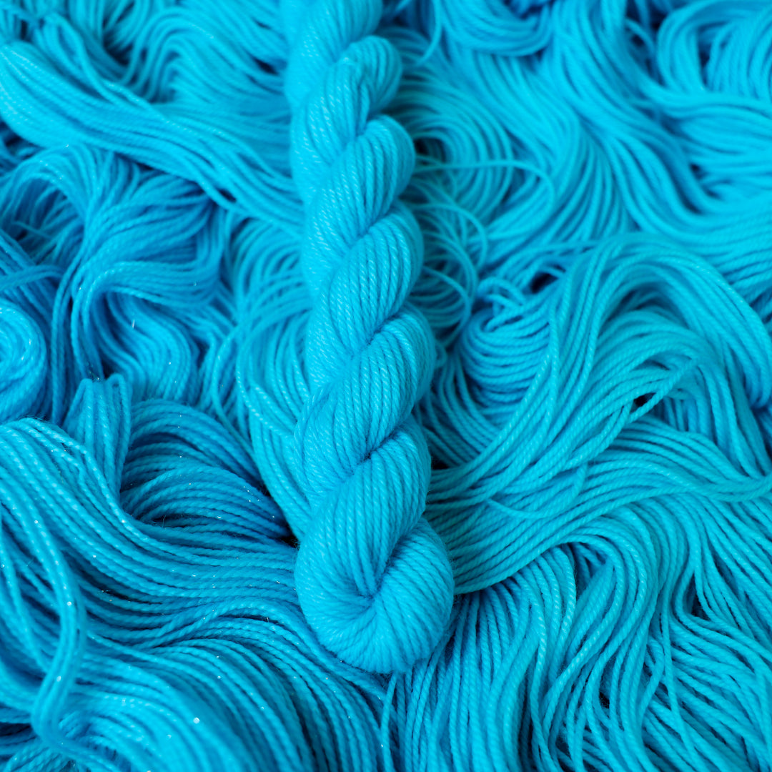Fingering mini teal blue colored yarn skein on top of unwound skeins of this same color way