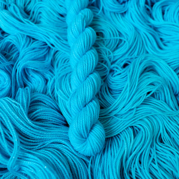Fingering mini teal blue colored yarn skein on top of unwound skeins of this same color way