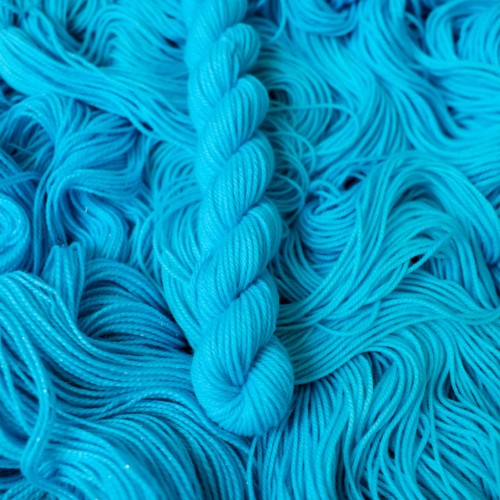 Fingering mini teal blue colored yarn skein on top of unwound skeins of this same color way