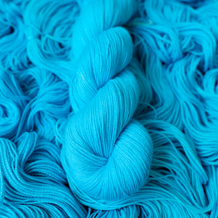 Fingering teal blue colored yarn skein on top of unwound skeins of this same color way