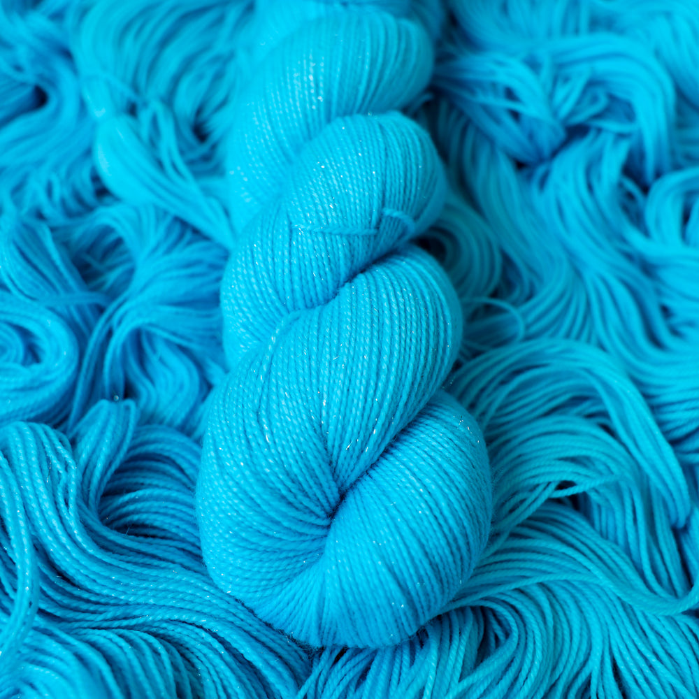 Sparkle fingering teal blue colored yarn skein on top of unwound skeins of this same color way