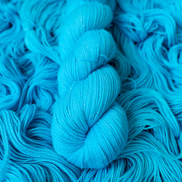 Sparkle fingering teal blue colored yarn skein on top of unwound skeins of this same color way