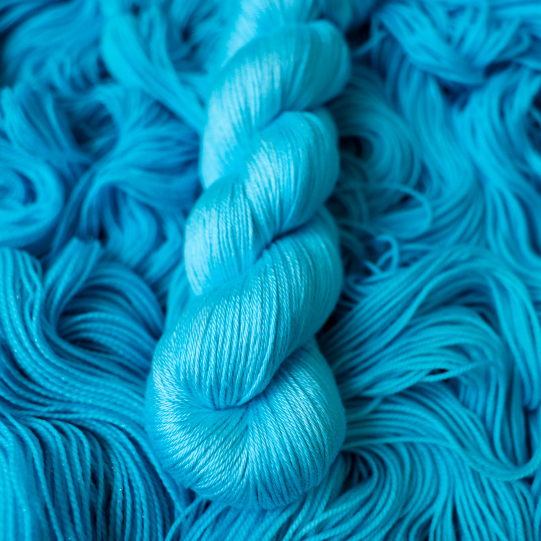 Silk teal blue colored yarn skein on top of unwound skeins of this same color way