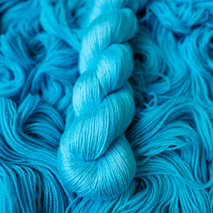 Silk teal blue colored yarn skein on top of unwound skeins of this same color way