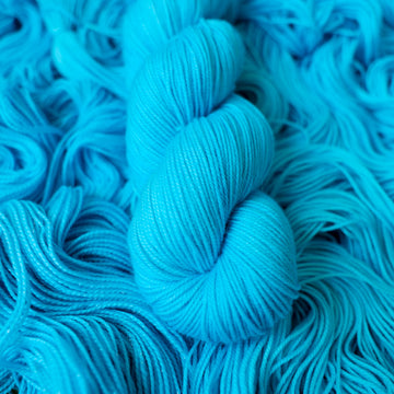 Sport teal blue colored yarn skein on top of unwound skeins of this same color way