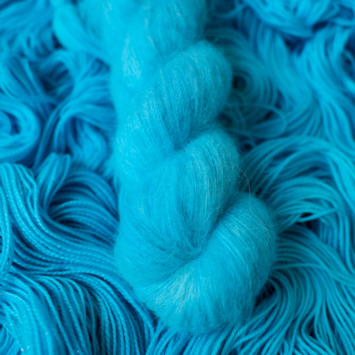 Suri alpaca teal blue colored yarn skein on top of unwound skeins of this same color way