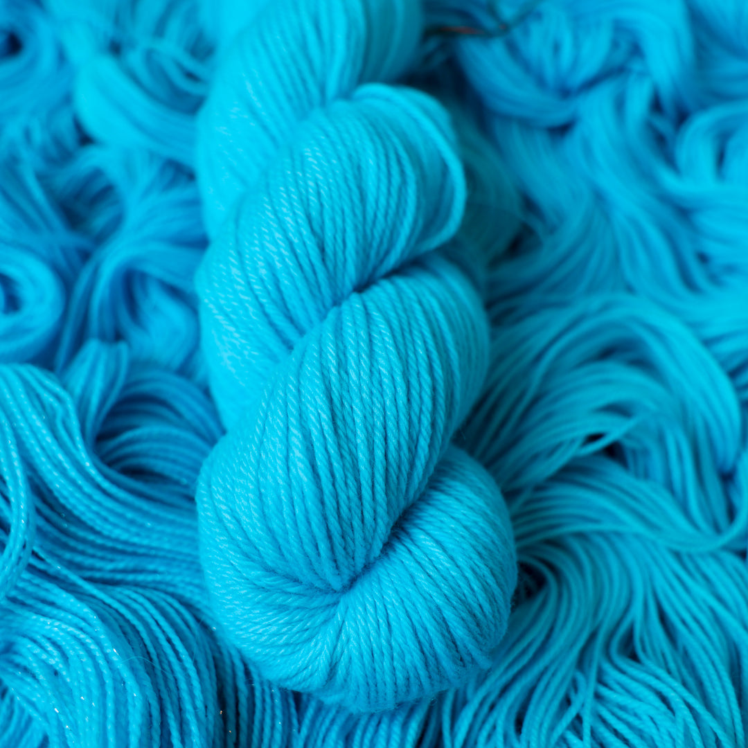 Worsted teal blue colored yarn skein on top of unwound skeins of this same color way
