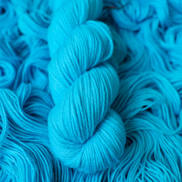 Worsted teal blue colored yarn skein on top of unwound skeins of this same color way