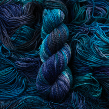 Bulky yarn colored with different shades of blue and some light bluish purple. Unwound weights of this same yarn is underneath this skein.