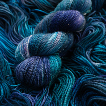 Sparkle yarn colored with different shades of blue and some light bluish purple. Unwound weights of this same yarn is underneath this skein.