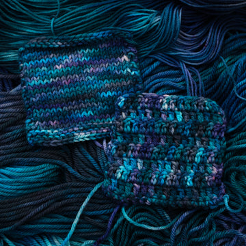 Crochet and Knit swatches colored with different shades of blue and some light bluish purple. Unwound weights of this same yarn are underneath these swatches
