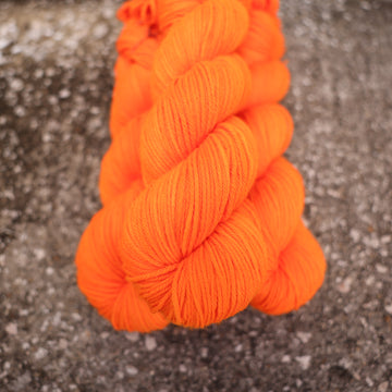 A couple of vibrant orange Worsted yarn skeins on top of gravel.