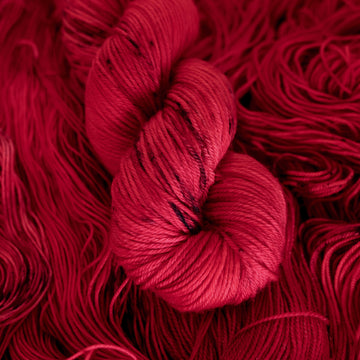 A vibrant red colored Worsted yarn with some dark speckles, on top of an unwound version of that same yarn.