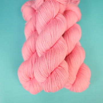 A light pink colored Worsted yarn on top of a light blue background.