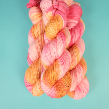 A couple of Worsted yarn skeins that are colored with a light pink, yellow, and orang e, on top of a light blue background.